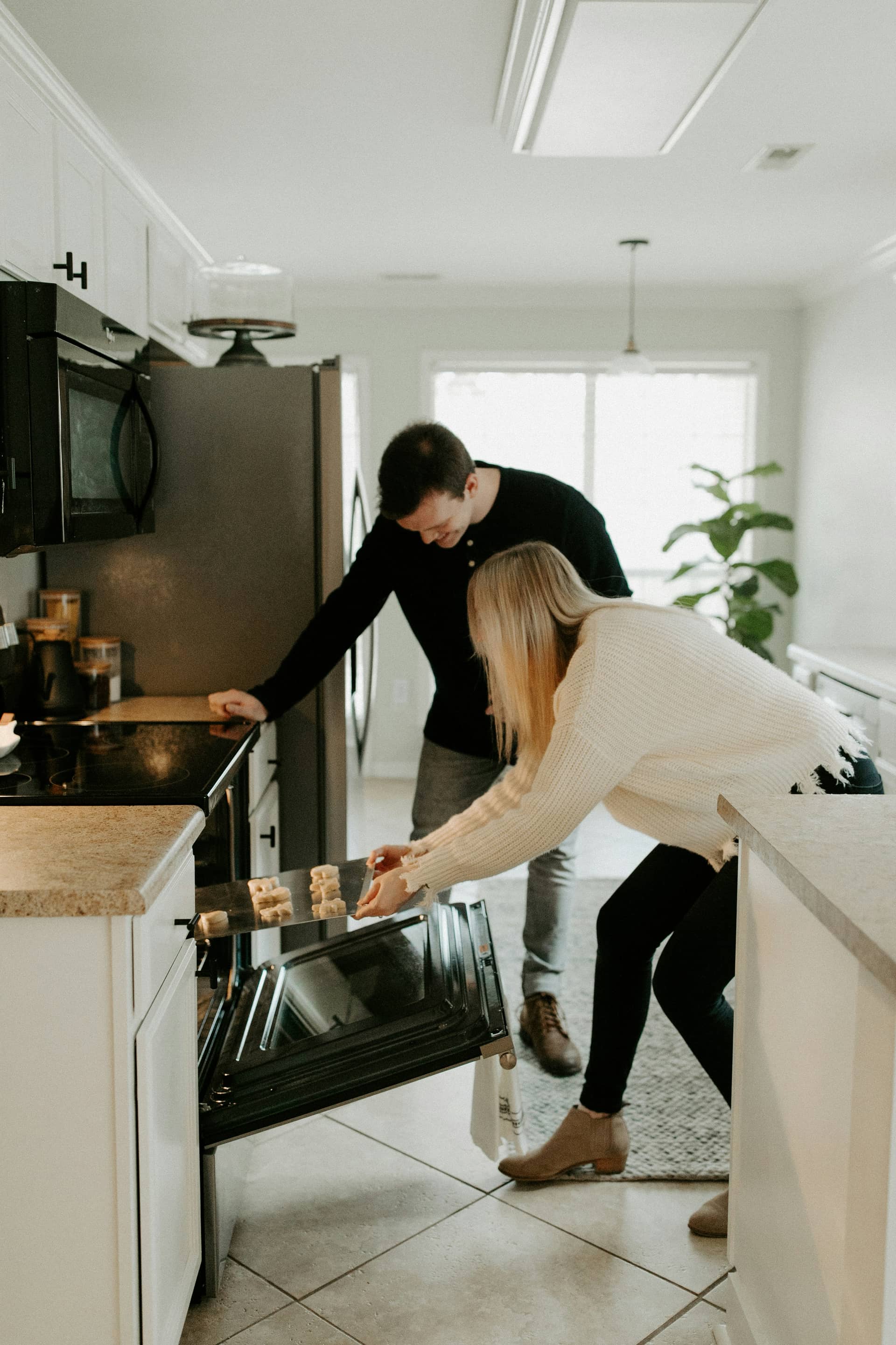 Two friends pulling cookies from the oven in a bright kitchen.