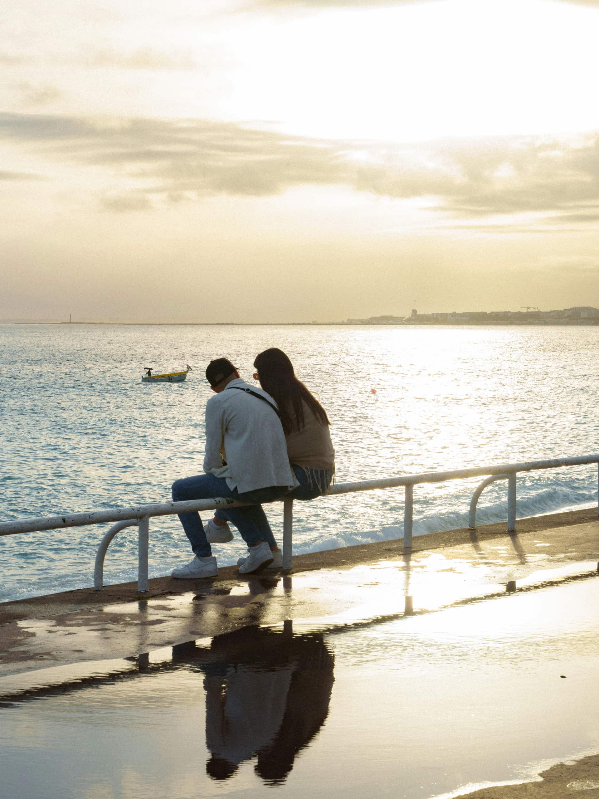 Two friends sitting close together by the sea at golden hour.