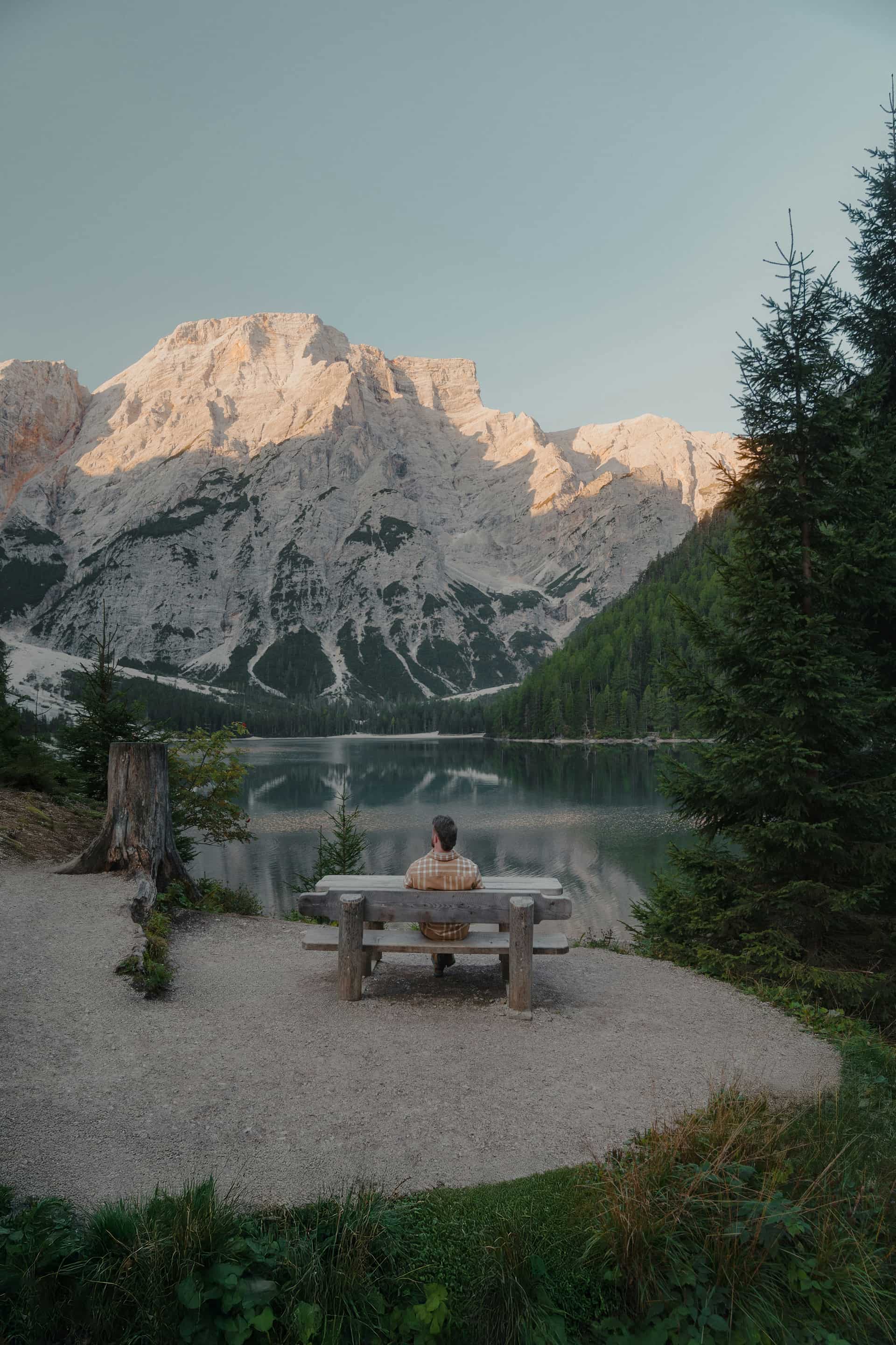 A person sitting alone on a bench facing a still lake at first light.